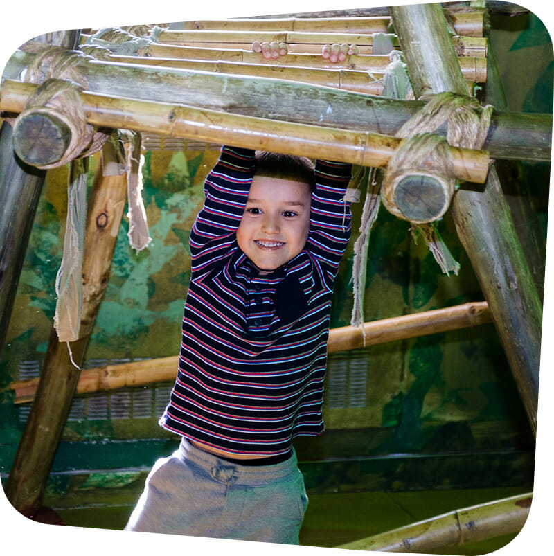 child hanging from bamboo bars in Great Explorations exhibit.