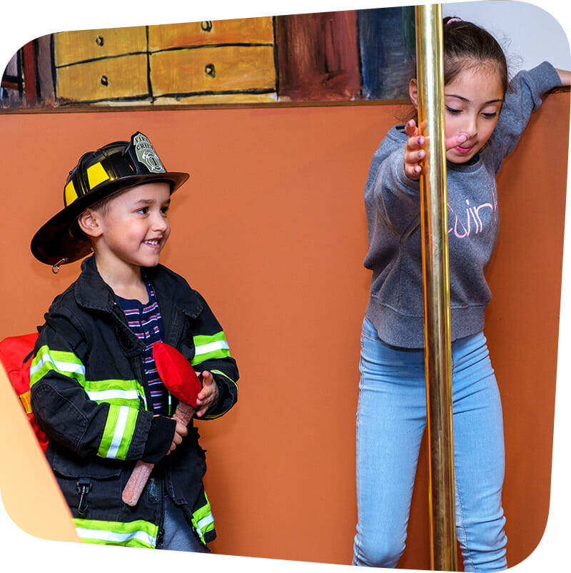 Children playing in firefighter exhibit in firefighter gear.