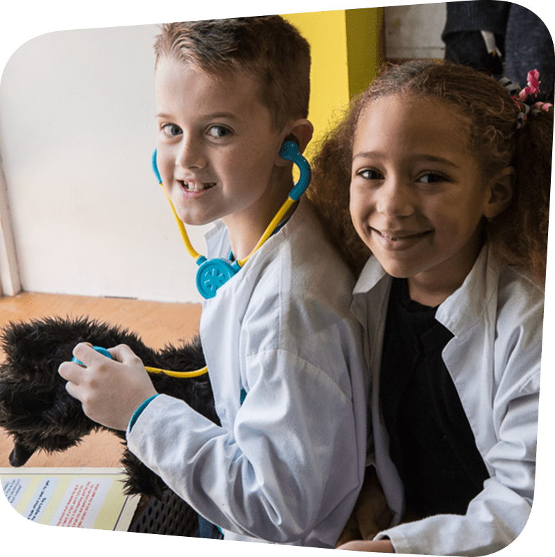 Two children smiling with white doctor coats on.