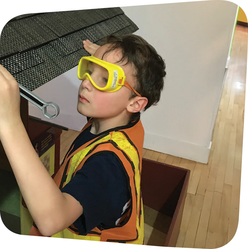 Child with construction goggles and vest playing in House About it Exhibit.