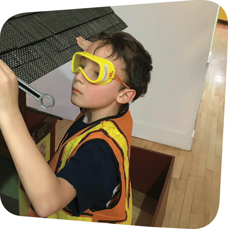 Child with construction goggles and vest playing in House About it Exhibit.