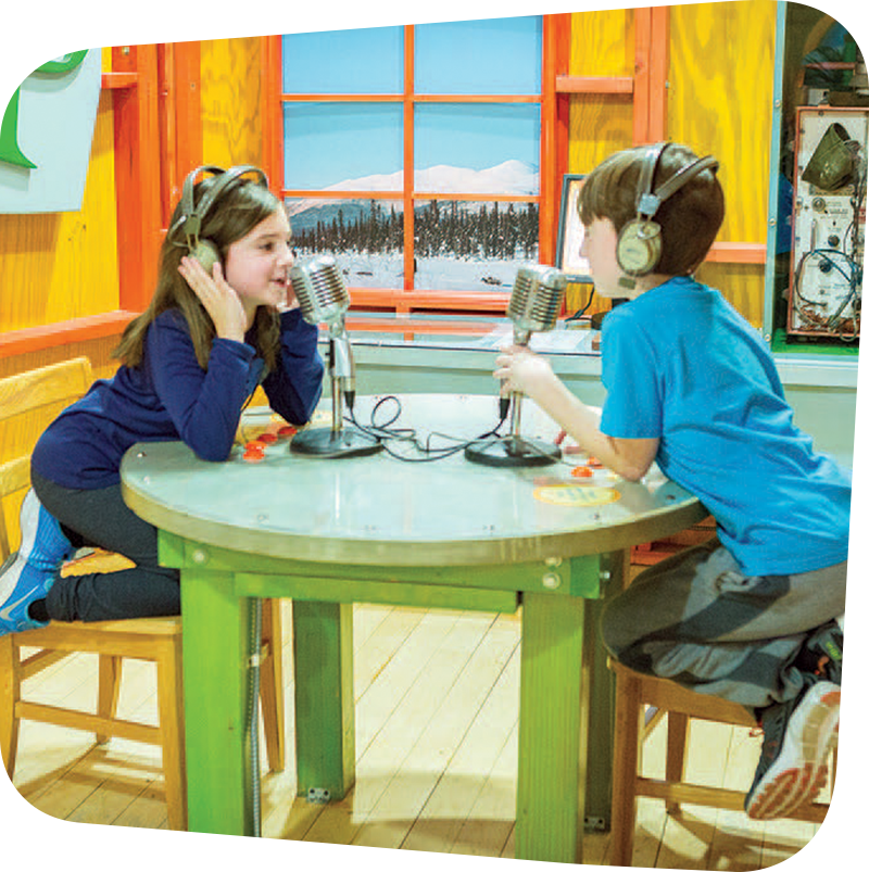Two children with headphones speaking into microphones.