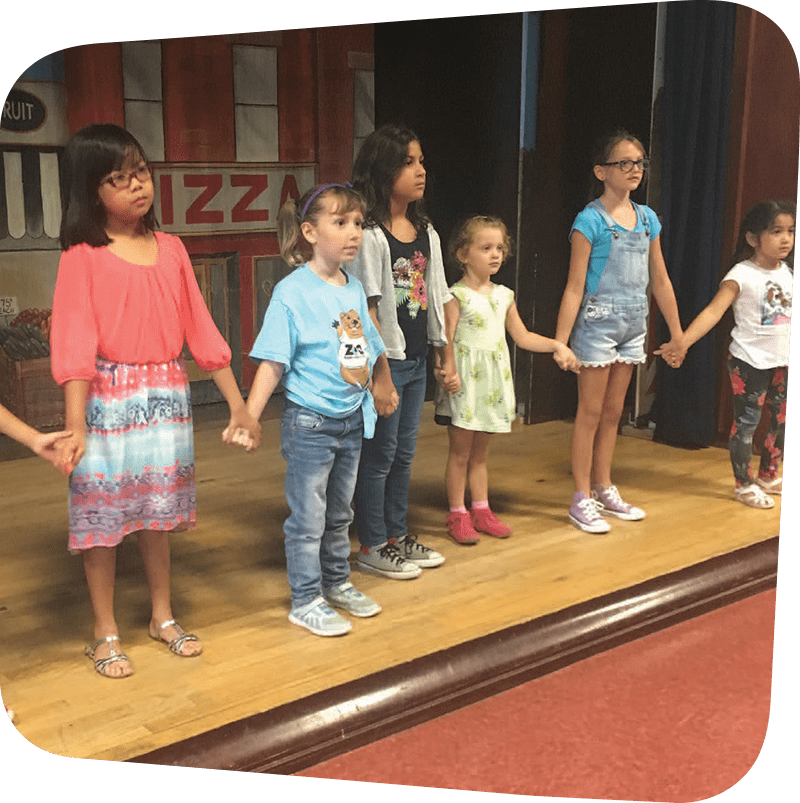 Children holding hands on stage during performing arts workshop.