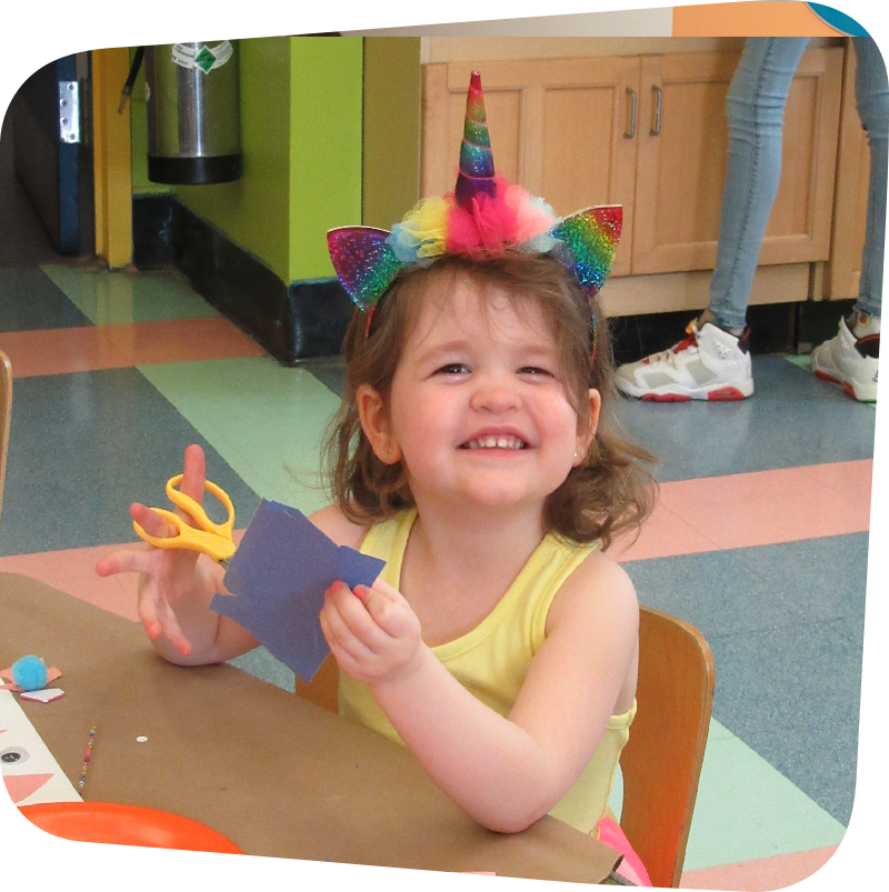 girl smiling while cutting blue paper with yellow scissors