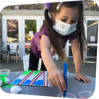 child reaching across table dipping brush in paint