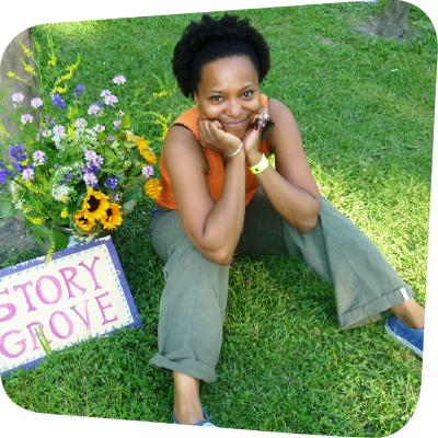 April Armstrong sitting on the grass in a Story Grove with her hands on her knees smiling up at the camera