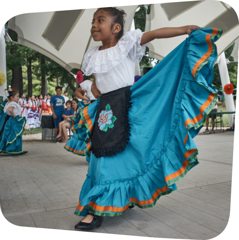 Child Dancing in Traditional Mexican Dress of a white blouse and aqua skirt with a black apron that has a flower on it.