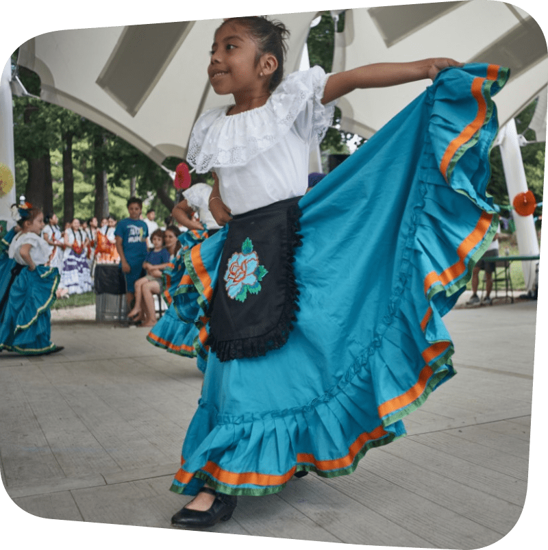 Child Dancing in Traditional Mexican Dress of a white blouse and aqua skirt with a black apron that has a flower on it.