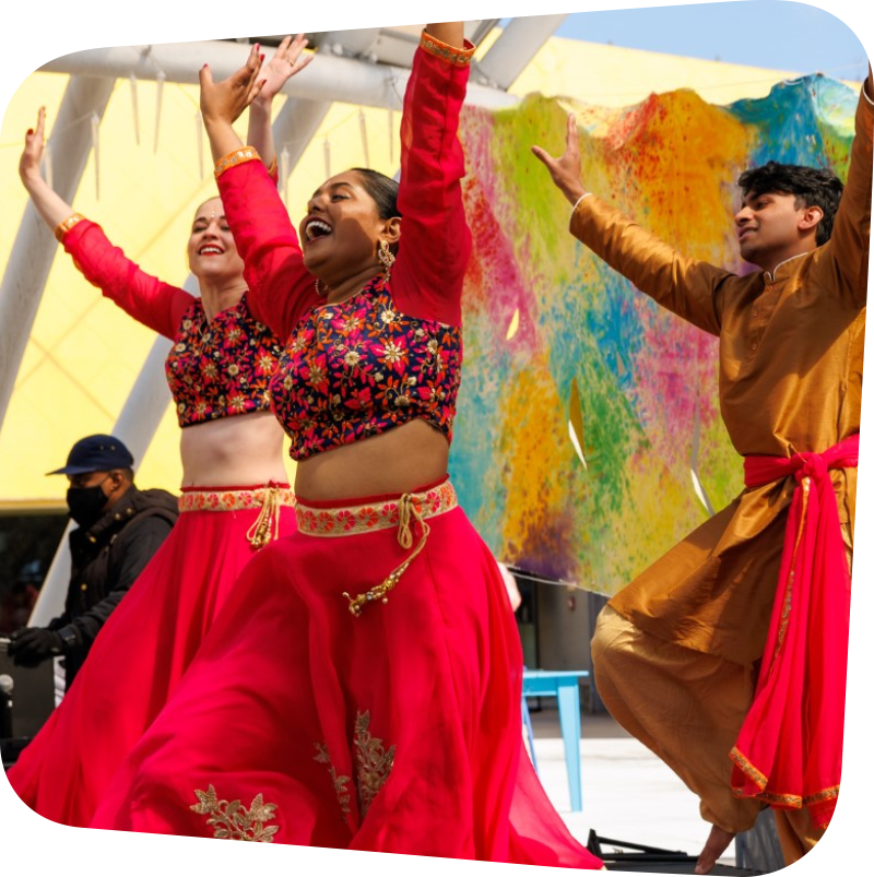 Dancers in bright red dress dancing with hands in the air in a Holi celebration
