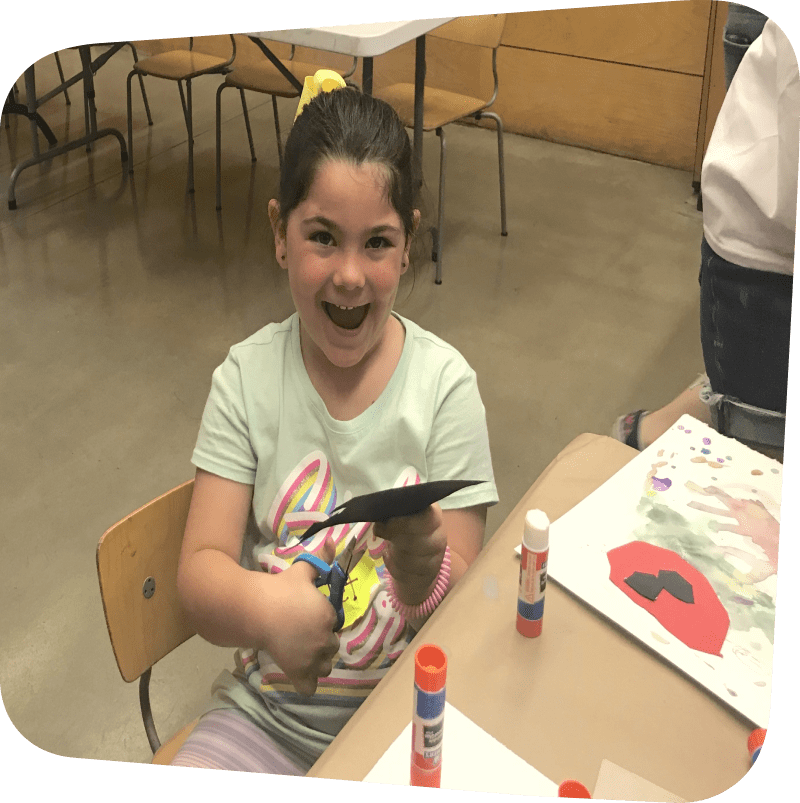 smiling child cutting out artwork in classroom setting