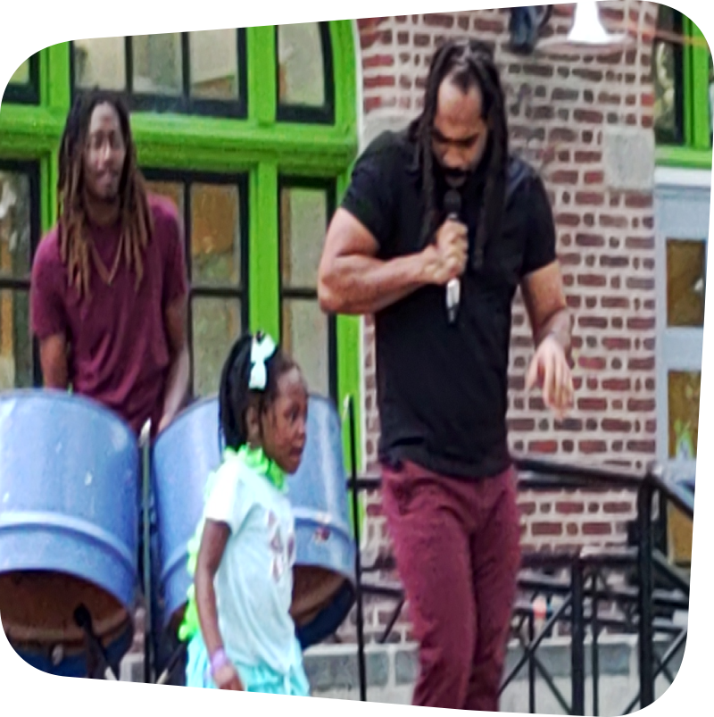 man playing steel drums behind young girl dancing and man with microphone dancing