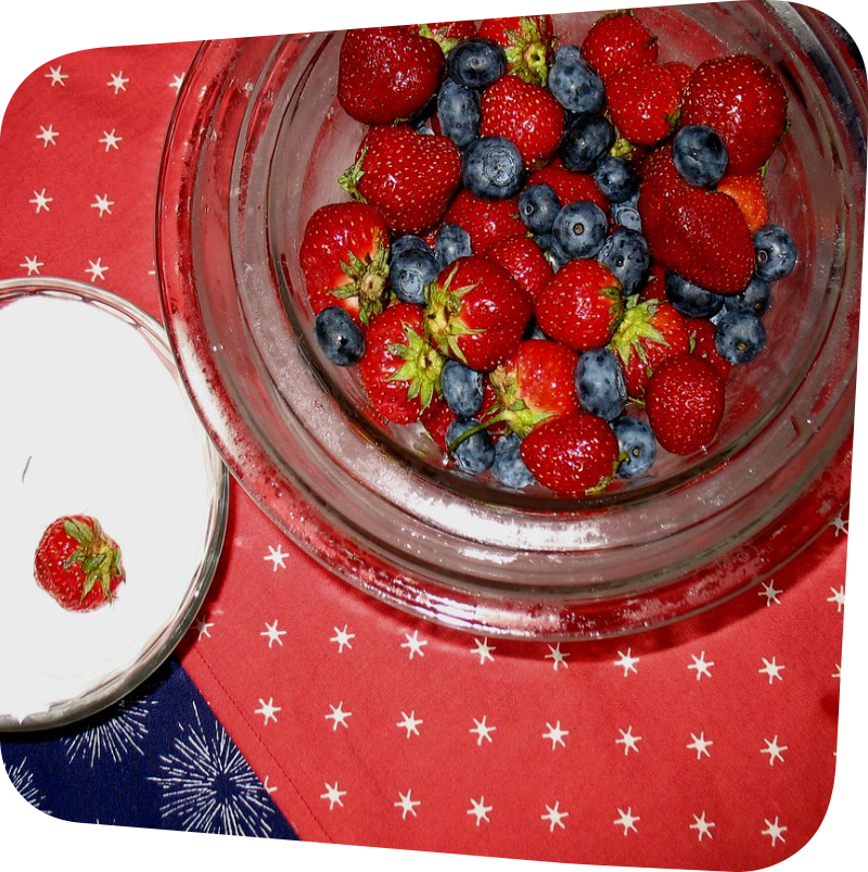 two bowls: one of white yogurt and one of whole strawberries and blueberries