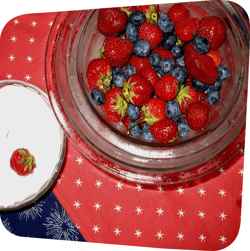 two bowls: one of white yogurt and one of whole strawberries and blueberries