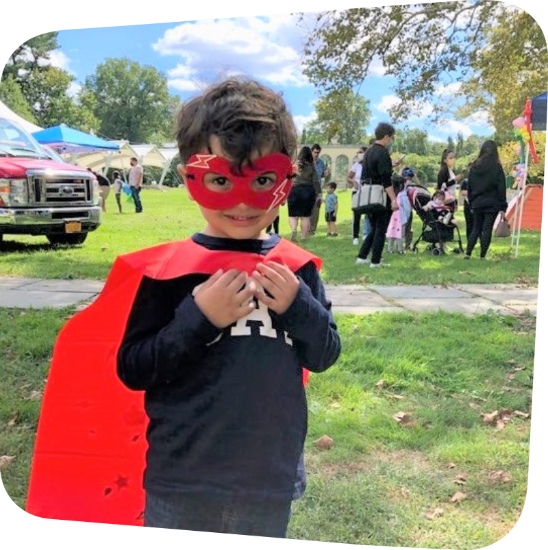 child in superhero cape in meadow in front of parked emergency vehicle and info booth