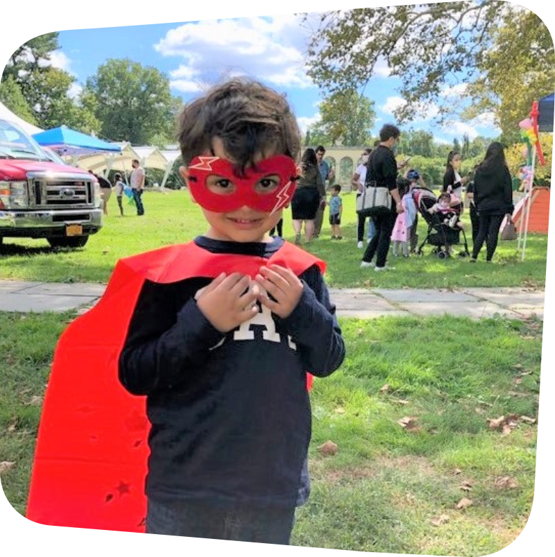 child in red superhero cape in meadow in front of parked emergency vehicle and info booth