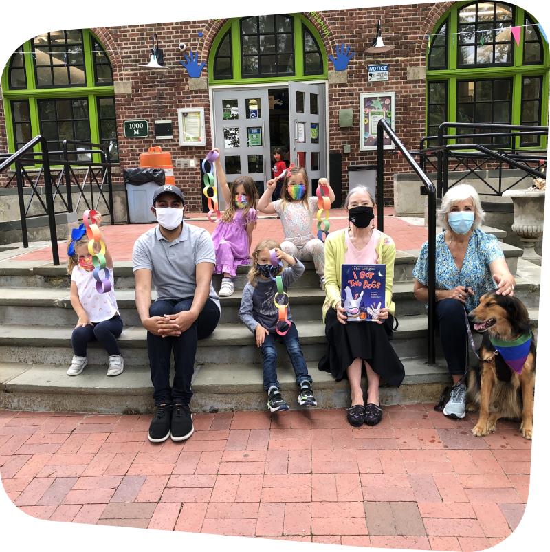 children, staff and volunteers sitting on the front steps of the museum with a dog displaying a children's book and crafts they've made