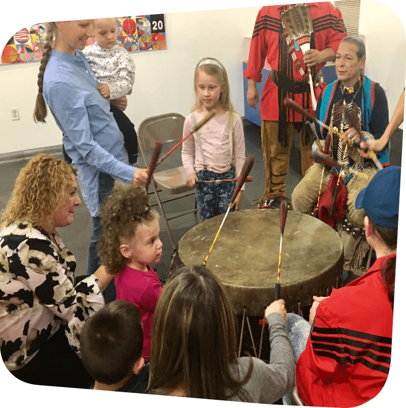 children and parents surrounding representatives from the Red Storm Drum and Dance Troupe with large drum in the middle