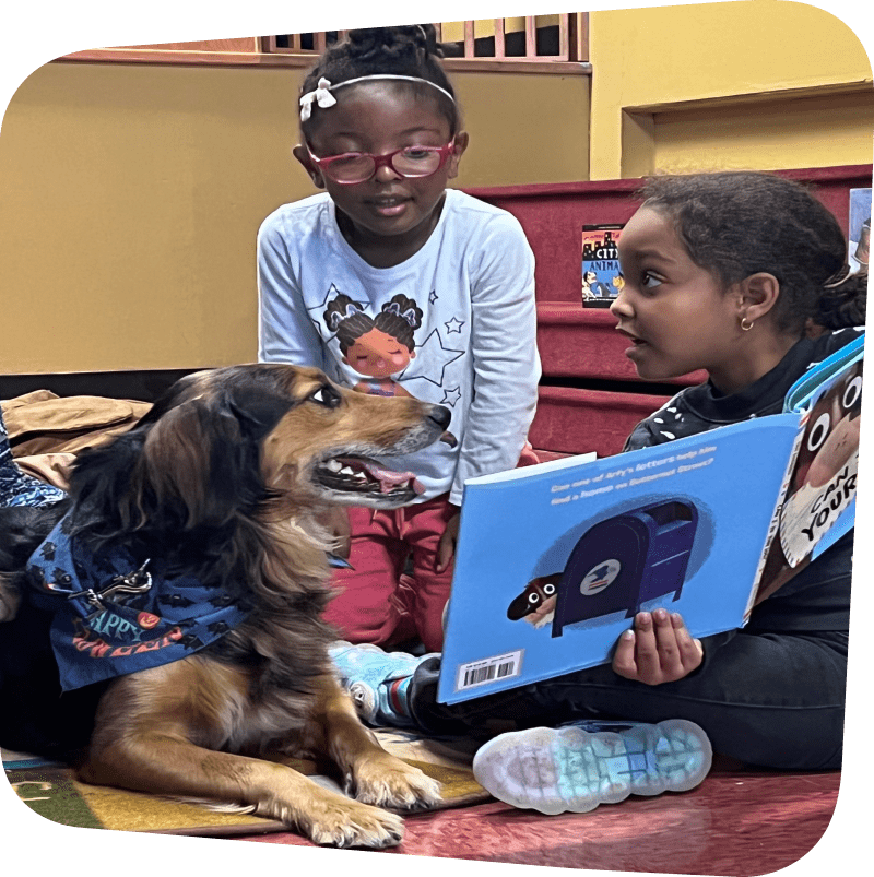 two young children sitting on the floor reading a picture book to a dog