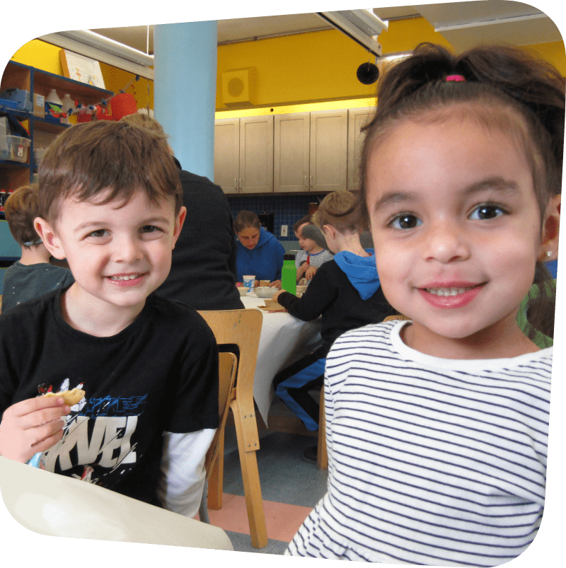 two children smiling at the camera while preparing their Kidz Cook recipe