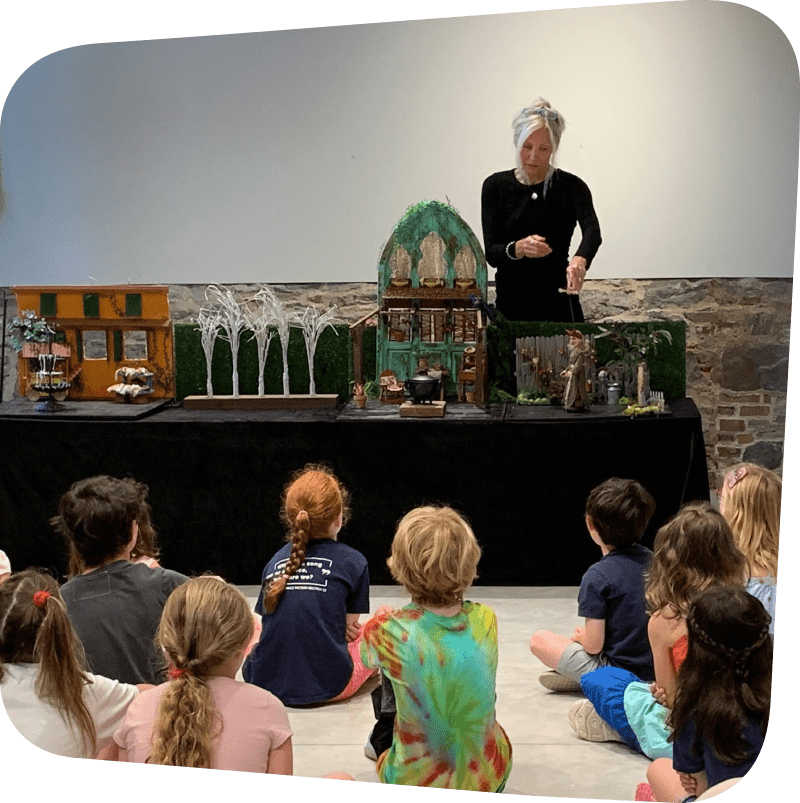 Kim Profaci featured performing "Strega Nona" with marionette puppets in front of a crowd of children