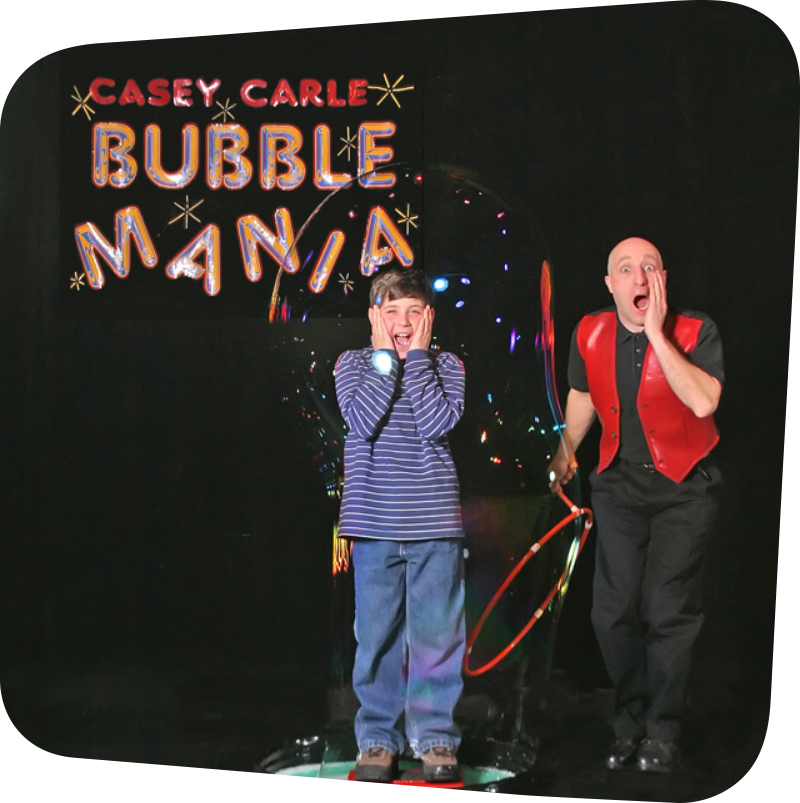 Casey, Bubble Mania entertainer, creating a bubble around a child. Both are seen making a shocked face.