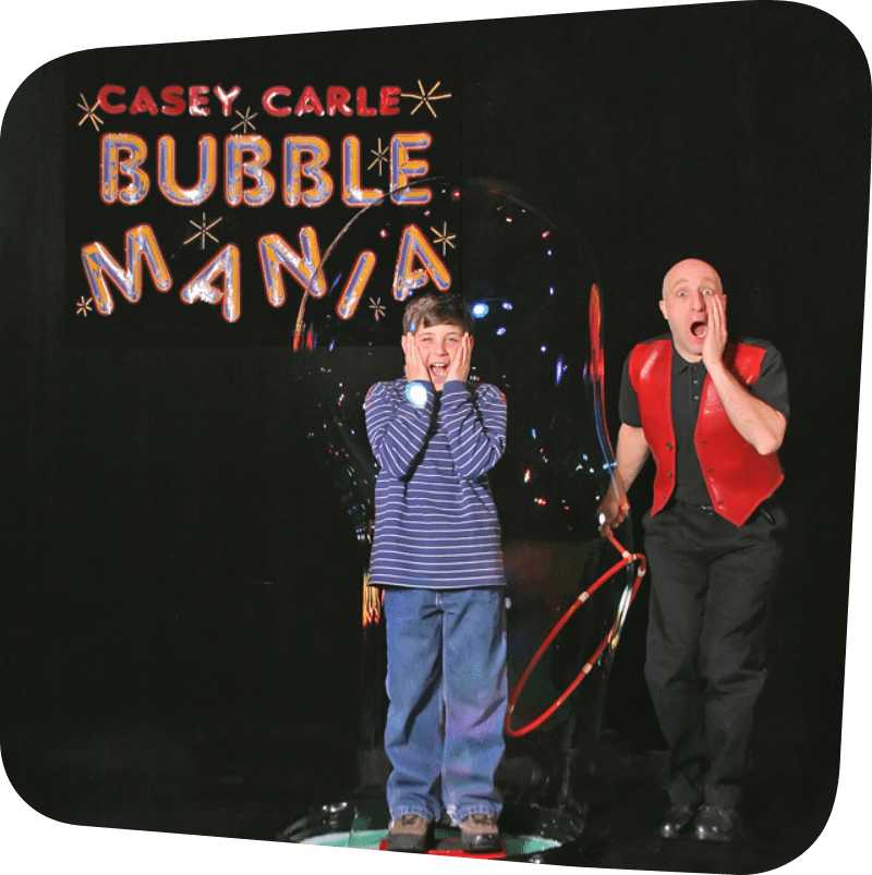 Casey, Bubble Mania entertainer, creating a bubble around a child. Both are seen making a shocked face.