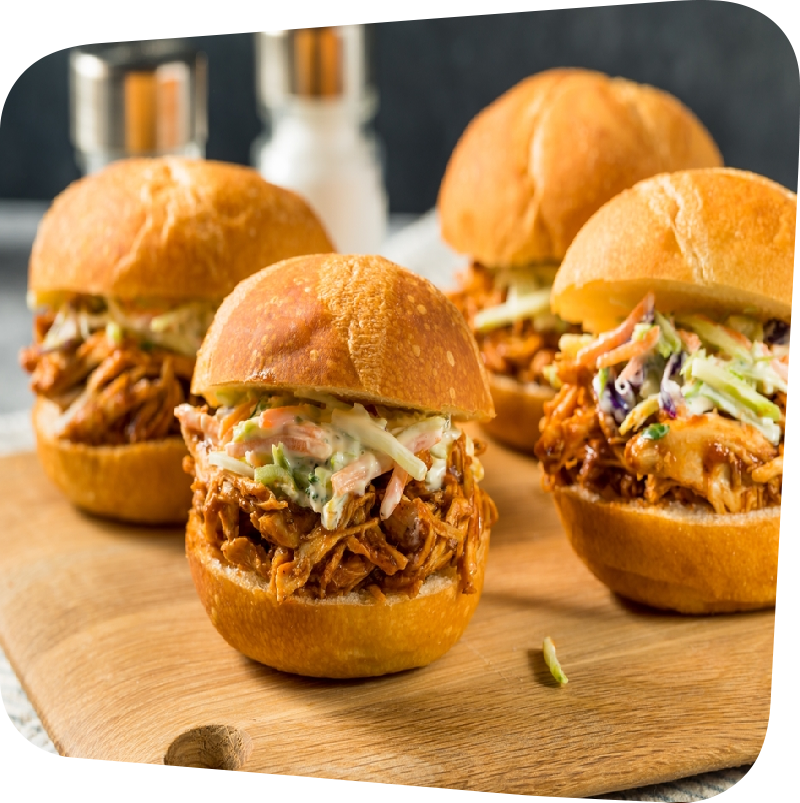 Four BBQ sliders with slaw on a butcher block slab
