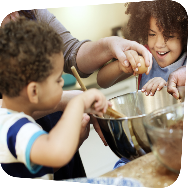 children gleefully helping an adult add ingredients to a bowl for mixing