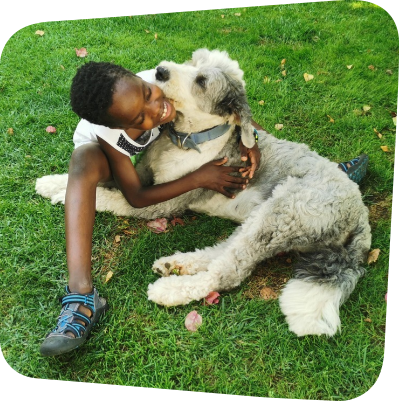 child featured hugging a white and grey dog while sitting on the grass