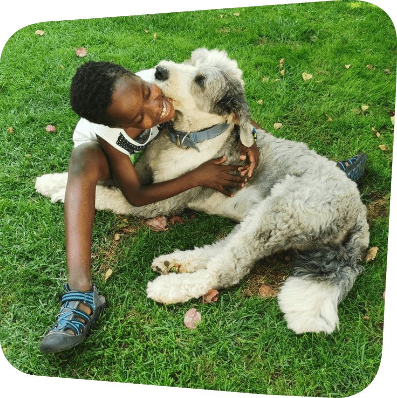 child featured hugging a white and grey dog while sitting on the grass