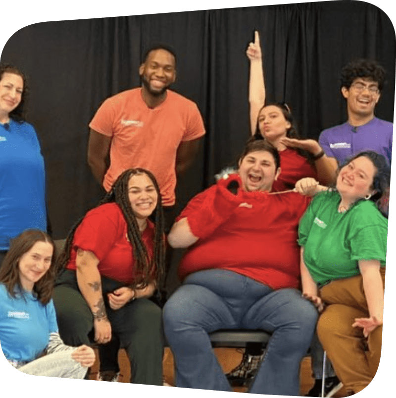 Actors in the production in colorful shirts surrounding Alex the puppet