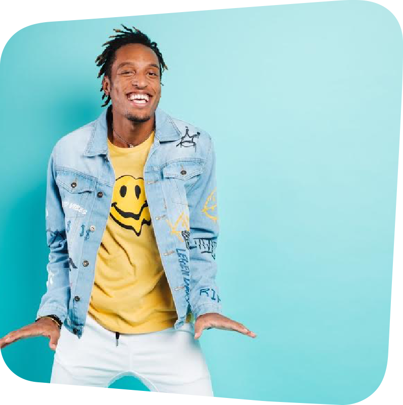 AY Young in a yellow smile face shirt and jean jacket against a blue background