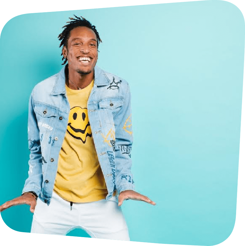 AY Young in a yellow smile face shirt and jean jacket against a blue background