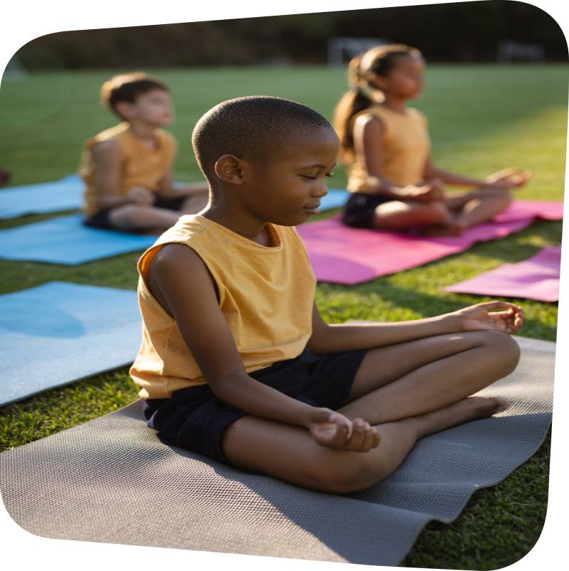 children sitting on mats on the meadow in traditional yoga meditative pose