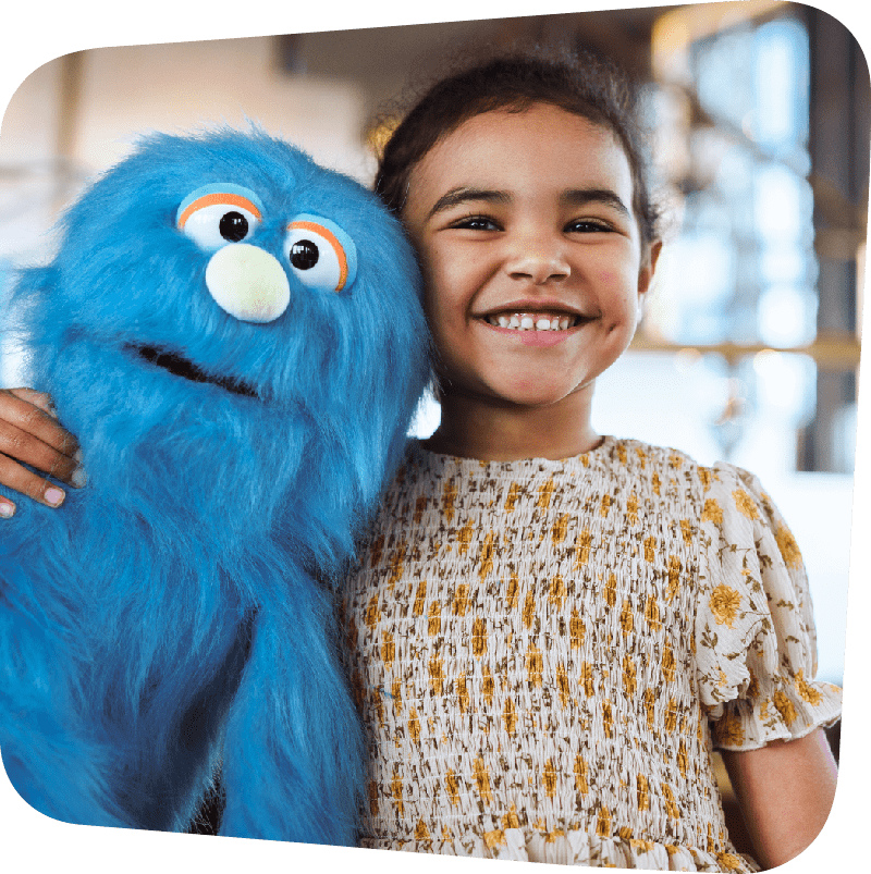child smiling and hugging a blue monster like puppet