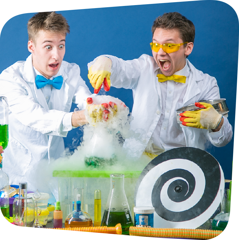 two young scientists with colorful bowties are astonished by what is emerging from a bubbling and seemingly steaming flask