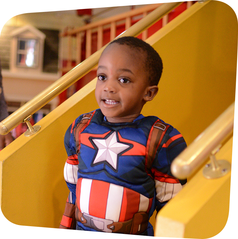 Child in superhero costume standing on the stairs to the firetruck