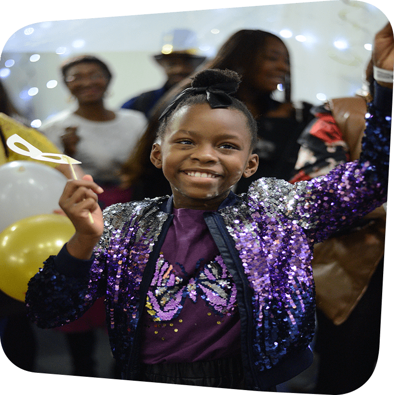 smiling child in a sparkly outfit in the midst of a baloon drop