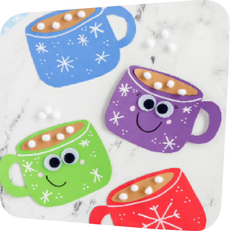 Four hot cocoa magnet crafts on a white countertop. Top left: blue mug with white snowflakes, fake brown "hot chocolate and fluffy white marshmallows" inside. Underneath, from right to left going down: purple, green, and red hot chocolate magnet mugs. The purple and green mugs have googly eyes and smiles.