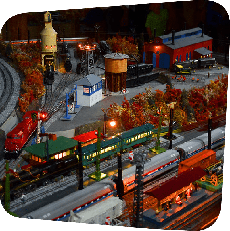A model train village with trains in the station and the lamposts alight