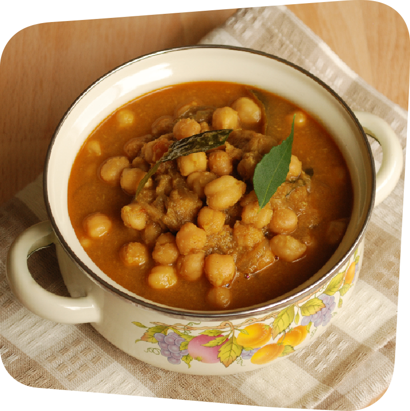 Chickpeas in a brown curry soup served in a white porcelain serving dish on top of a brown and white checkered towel and brown wooden table.