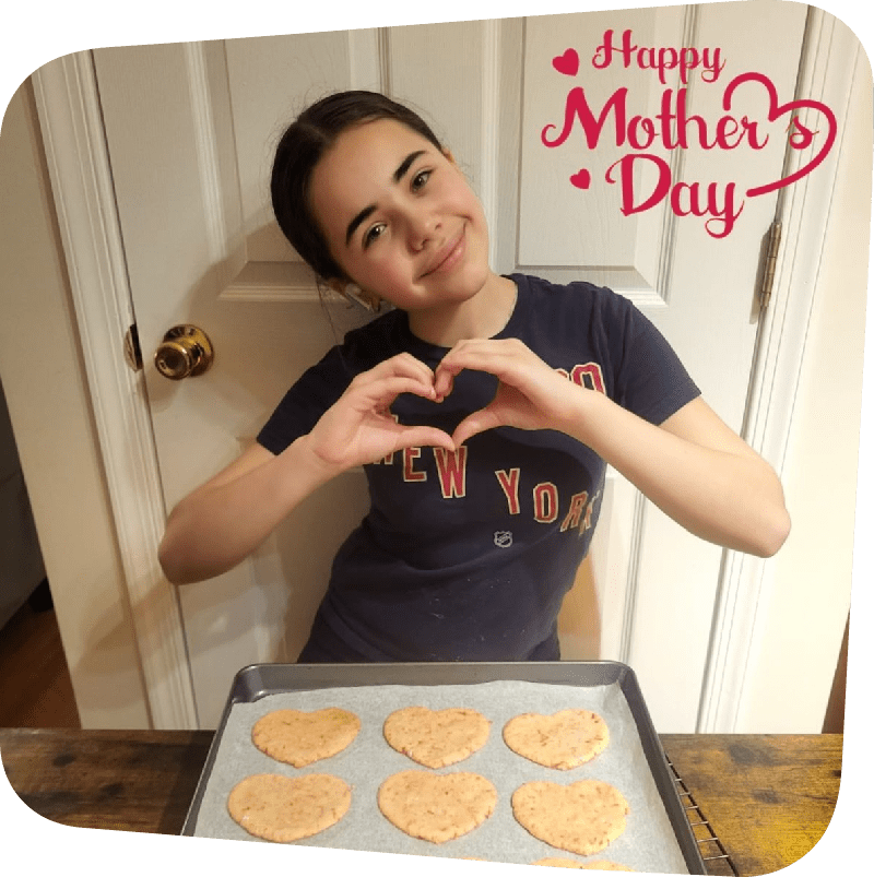 Maddison French making a heart shape with her hands, standing behind a try of freshly baked cookies
